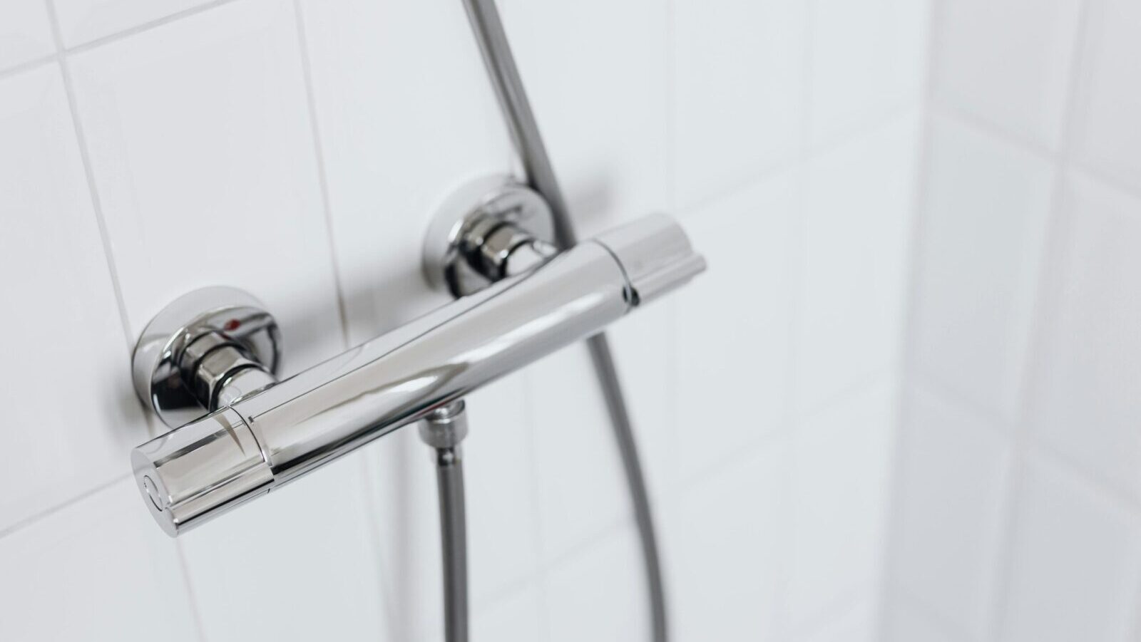 Modern chrome shower faucet on white tiled wall, elegant and clean design.